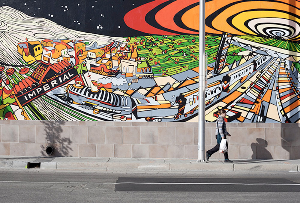 Photo of person walking infront of a colorful and fun mural of downtown Albuquerque.
