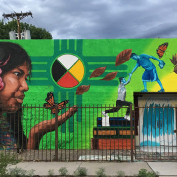girl discovers butterfly against New Mexico symbol mural